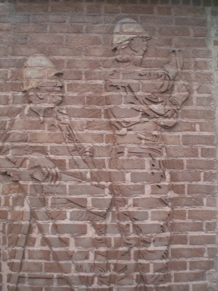 one seated (left) and one standing (right) worker, done in relief on a brick wall